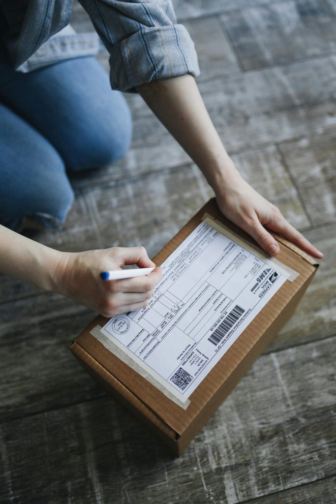 Hands writing label on a cardboard box, ready for shipment or mailing.